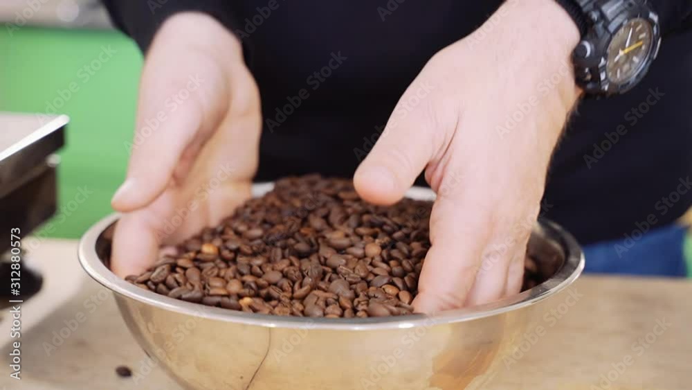 Male hands mix roasted coffee beans in a metal bowl. Male hands mix roasted coffee beans in a metal bowl.