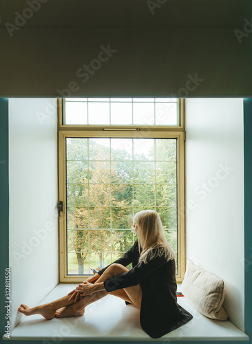 Beautiful blond girl sitting on window sill