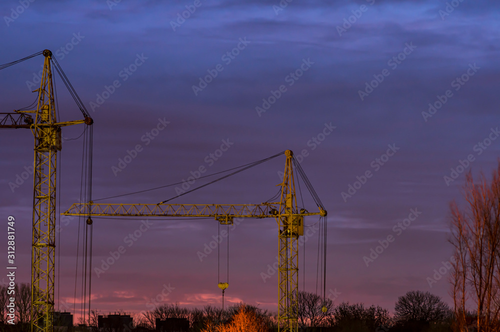 Two tower cranes against the sunset sky