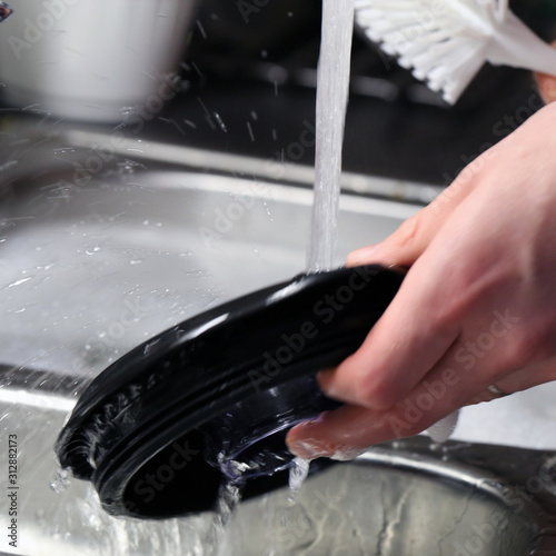 Doing dishes after cooking at home. Caucasian male doing the dishes. Closeup image. In this photo there is a top of smoothie blender being washed with some soup bubbles and running water. Color photo.