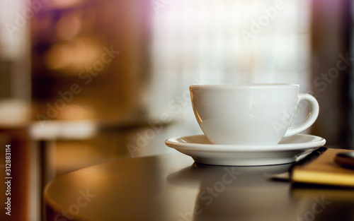 Close-up white cup of coffee with notebook on desk.  Background vintage light