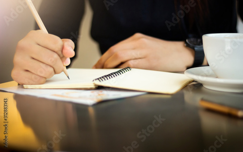 Close-up. Young female working and writing notebook with cup of coffee on desk