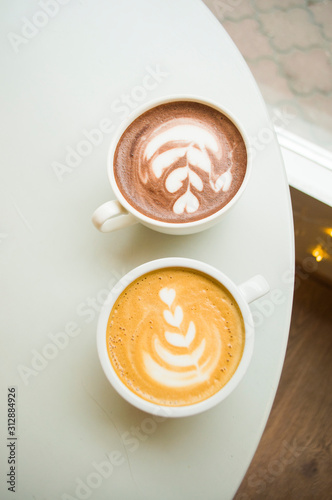 Two cups of cappuccino and hot cocoa with beautiful latte art on a grey wooden table in a cafe with copyspace.