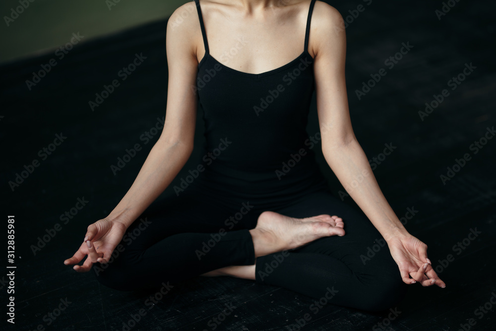 Obraz premium Asian girl sitting in lotus position in yoga class in a black tank top in black leggins