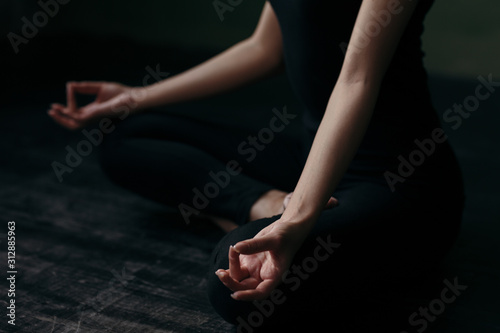 Asian girl sitting in lotus position in yoga class in a black tank top in black leggins