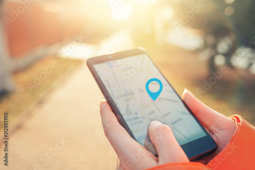 Concept of Internet maps and navigation. Women's hands hold a smartphone with a map application, and a marked icon of the location. Light