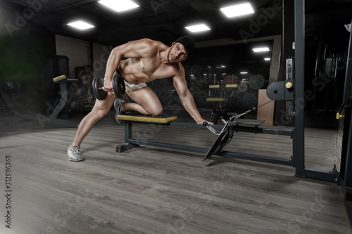 Muscular strong athletic bodybuilder doing one-arm dumbbell rows on bench in gym. Concept sport photo with copy space