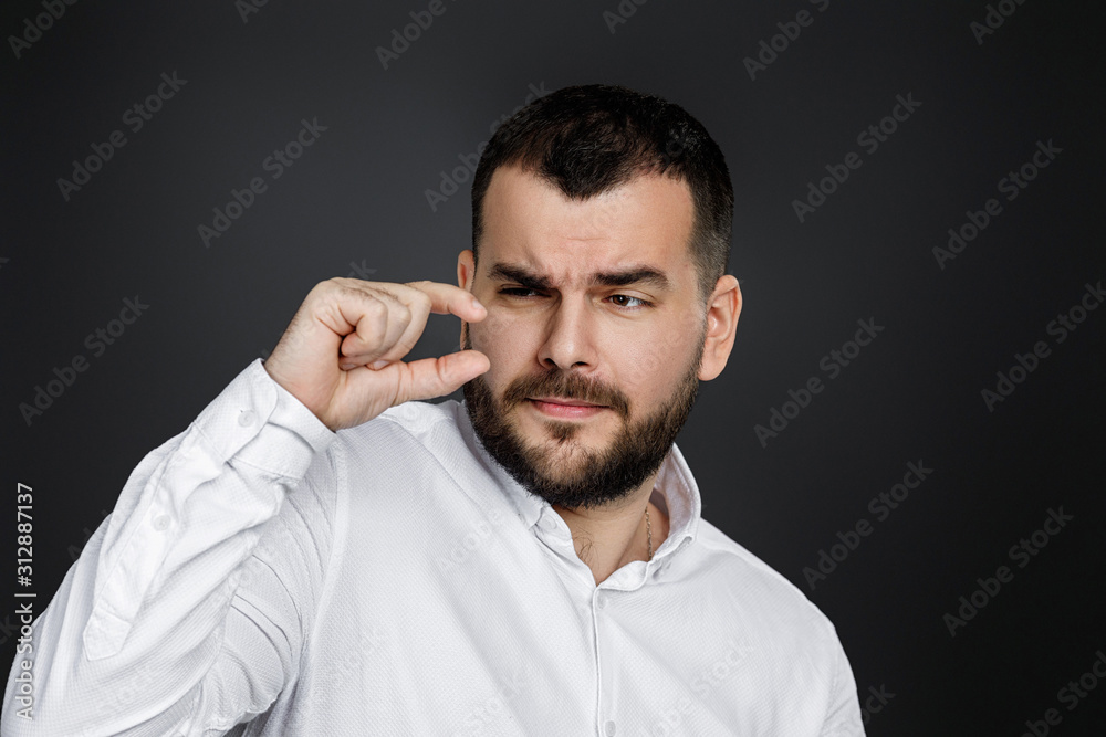 Obraz premium handsome bearded man holding two hands in front of him showing small size on black background