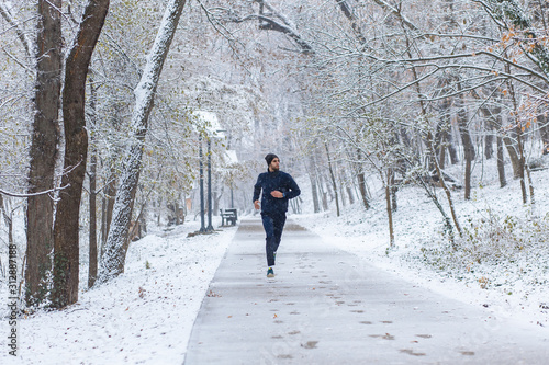 Young man running in city park at cold winter day.	