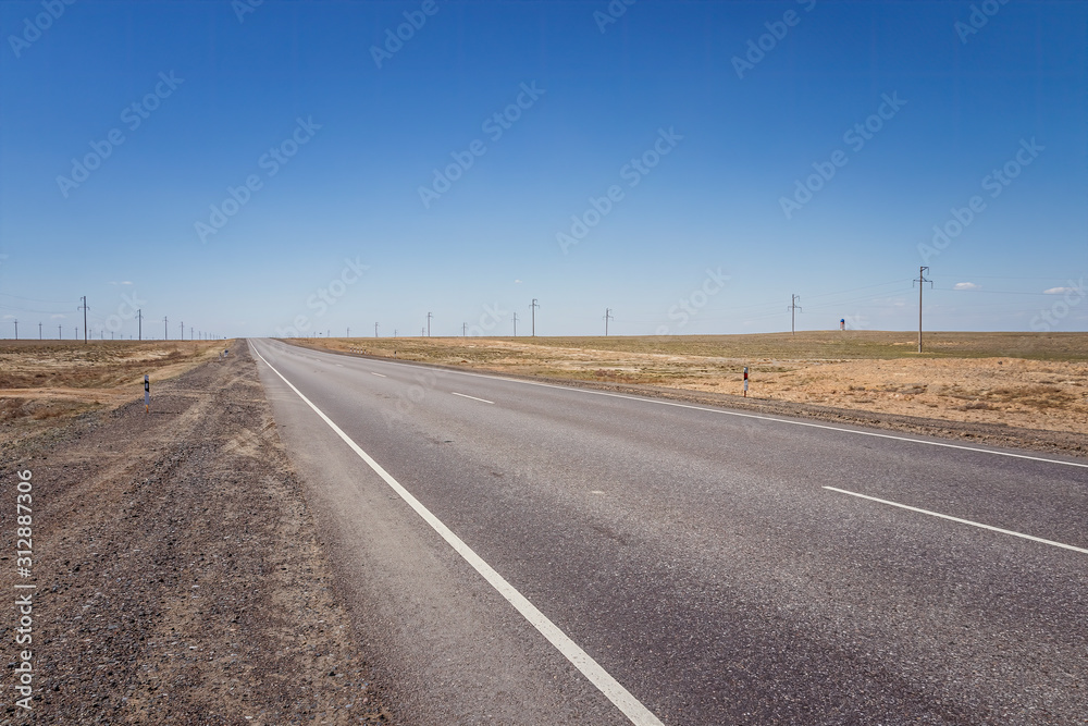 Modern two-lane asphalt desert road against a blue sky in Kyzylorda Oblast of Kazakhstan