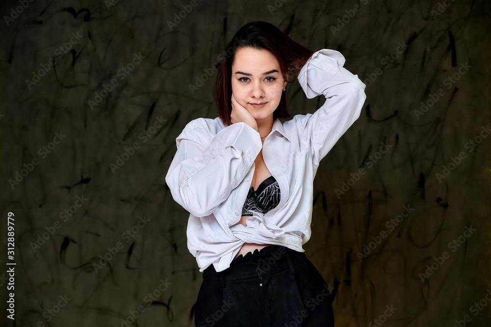 Portrait of a pretty smiling brunette Caucasian female student girl in a white shirt on a gray background. Standing right in front of the camera in various poses. Portrait of a pretty smiling brunette Caucasian female student girl in a white shirt on a gray background. Standing right in front of the camera in various poses.