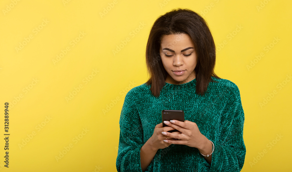 Young african american woman looking at screen of phone and smiling nicely while chatting