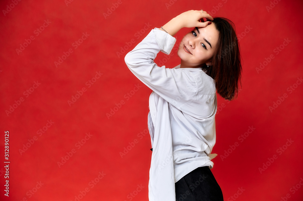 Portrait of a pretty smiling brunette Caucasian female student girl in a white shirt on a red background. Standing right in front of the camera in various poses. Portrait of a pretty smiling brunette Caucasian female student girl in a white shirt on a red background. Standing right in front of the camera in various poses.