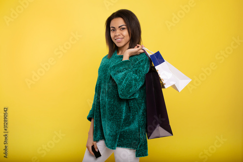 Portrait beautiful smiling african woman with shopping bags on yellow background.
