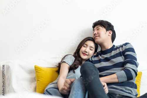 Asian young couples man and woman staying together in bed room. Girl putting head on boyfriend shoulder and closing eyes feeling love happy with smile face. Relationship of young girl and boy concept.