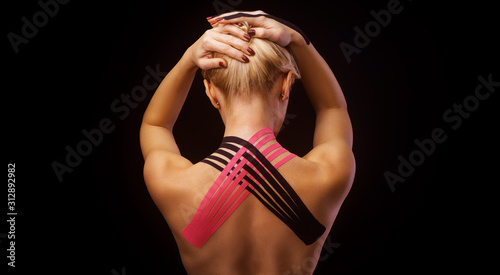 Beautiful young woman with kinesiotape on her neck area after injury on black background photo