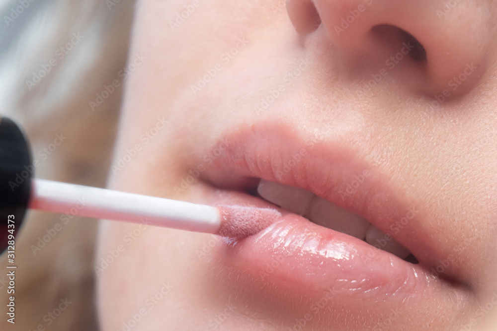 Naklejka premium girl paints her lips with lip gloss. Photo close-up
