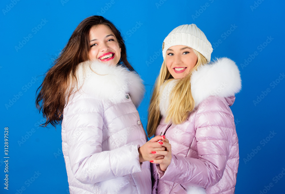 Fashion friends. Winter clothes. Women wear down jacket with furry hood.  Girls smiling makeup faces wear winter jackets blue background. Winter  season. Soft fur. For those wishing stay modern - Stock Image 