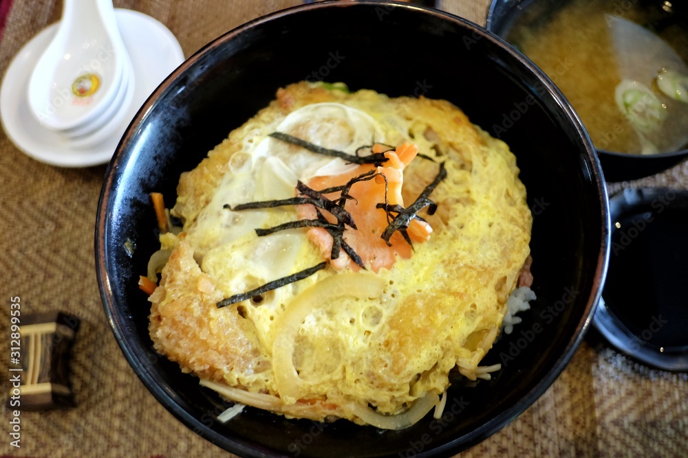 A black bowl of Katsudon menu,a famous Japanese food on wooden dinning table A black bowl of Katsudon menu,a famous Japanese food on wooden dinning table