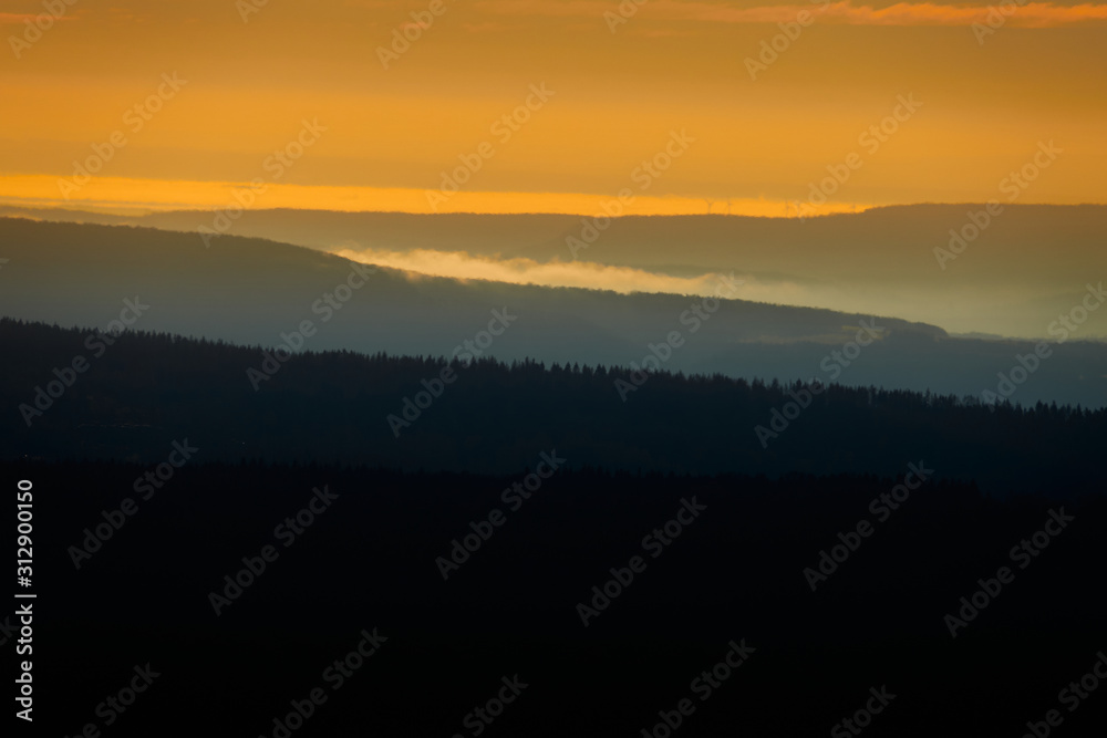 Gently undulating forest landscape in the Harz Mountains at sunrise with glowing sky and black forest Gently undulating forest landscape in the Harz Mountains at sunrise with glowing sky and black forest