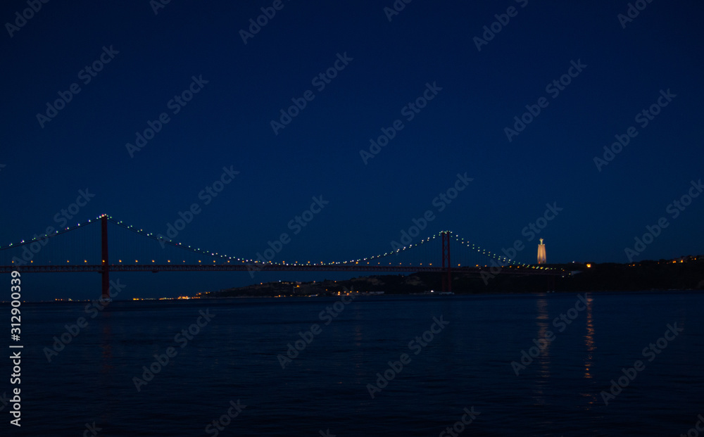 Fototapeta premium Portugal, Lisbon, panoramic view of night lights of Tagus bridge Lisbon, Ponte April 25th bridge over Tagus river, Lisbon on the Tagus river bank, Christ The King Statue Lisbon in night lights
