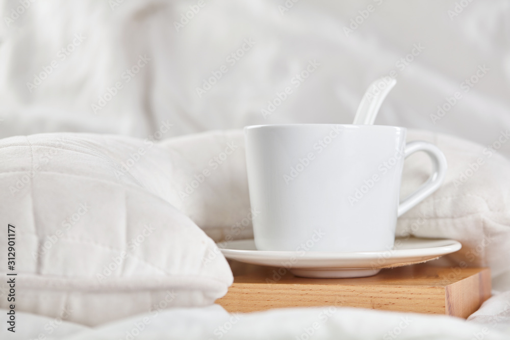 Cup of coffee on white bed on wooden stand. Close up.
