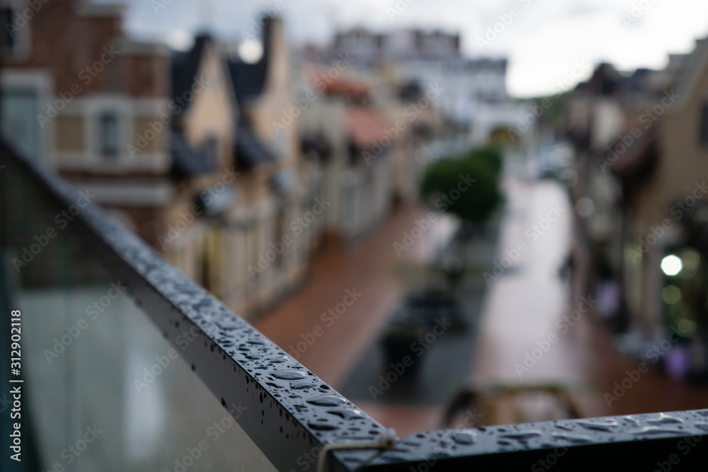 Rain drops on dark railing in autumn city in cloudy weather. on the blurry backdrop of the city streets.