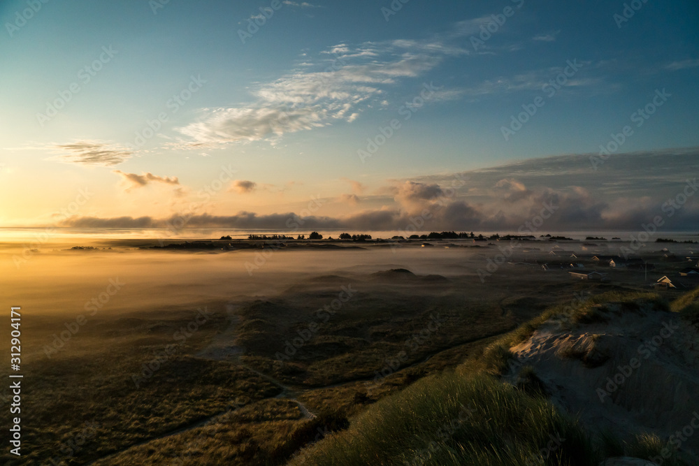 Landscape shot of holiday homes in the dunes Hvide Sande with beautiful sunrise and fog