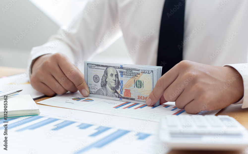 The businessman's hand is counting the dollar banknote at the desk. The businessman's hand is counting the dollar banknote at the desk.