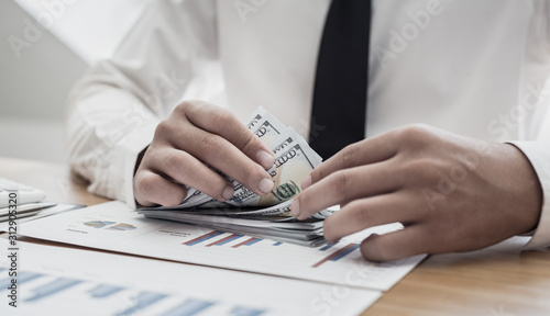 The businessman's hand is counting the dollar banknote at the desk.