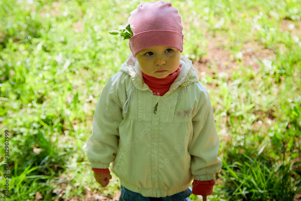 Portrait of a small girl in white dress and red hat in the park full of apple blossom trees in a spring day Portrait of a small girl in white dress and red hat in the park full of apple blossom trees in a spring day