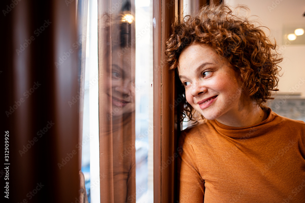 Young woman looking out window, view through glass, close-up. Beautiful woman at the window. Beautiful young brunette woman looking relaxed at home. Young woman looking out window, view through glass, close-up. Beautiful woman at the window. Beautiful young brunette woman looking relaxed at home.