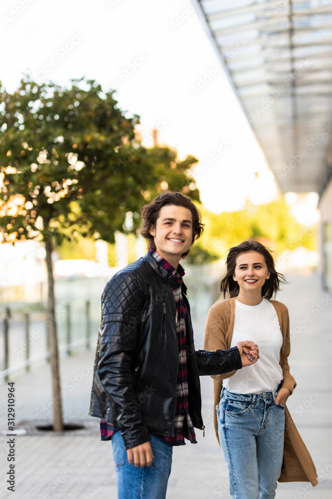 Happy to be together. Beautiful young couple holding hands and looking at each other with smile while walking through the city street