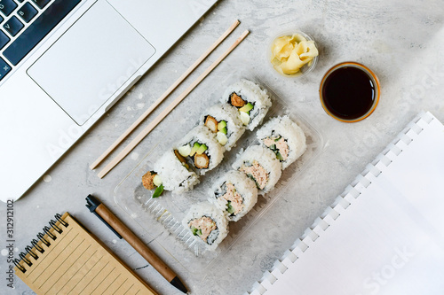 Food delivery. lunch box with sushi roll with tuna, avocado, cucumber and soy sauce on a gray office desk. takeaway lunch at the office. sushi menu delivery. Selective focus