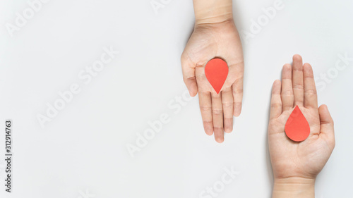 Obraz na plátne Blood donation - Human hand giving blood drop symbol to a hand on white background