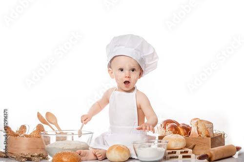 child with bread on bakery-like background wearing cook-hat. Little baker