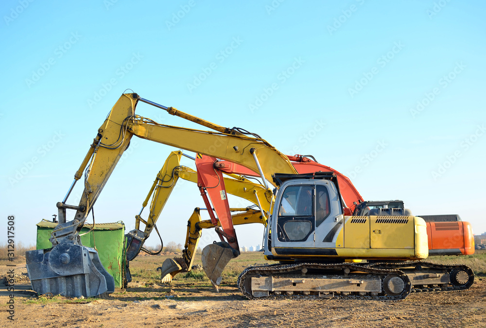 Group tracked excavators at a construction site. Special heavy construction equipment for road construction, road repair, laying of underground sewer pipes. Crushing bucket for crushing concrete. Group tracked excavators at a construction site. Special heavy construction equipment for road construction, road repair, laying of underground sewer pipes. Crushing bucket for crushing concrete.