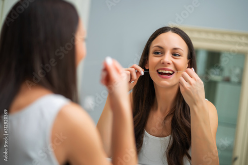 Young woman is using dental floss to clean her teeth.