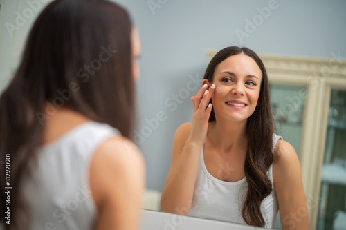 Portrait of young woman who is applying skin cream on her face.