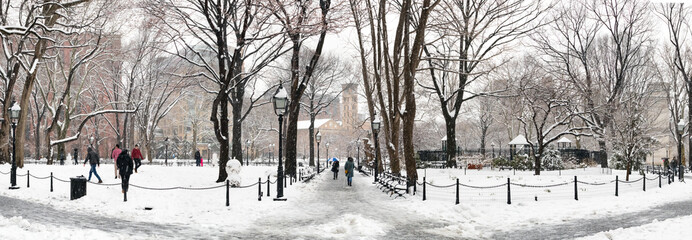Panoramic winter scene with people walking through the snow covered landscape of Washington Square Park in New York City