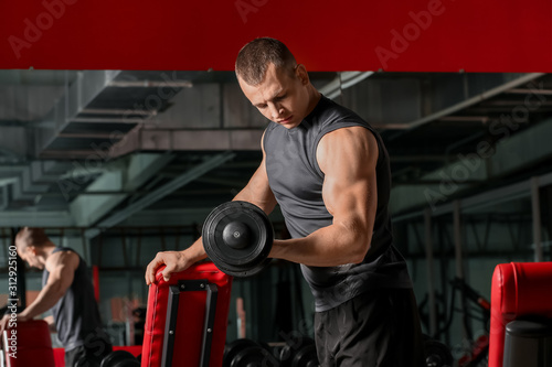 Sporty muscular man training with dumbbells in gym