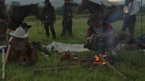 Cowboy groups stopped camping and rested and brewed coffee. And hold the kettle coffee pot poured into a glass. Some people are use knives to burn fire. Some people are rested at the horse saddles.