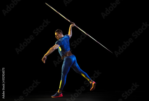 Male athlete practices in throwing javelin on black background in neon light. Professional sportsman training in action, motion. Concept of healthy lifestyle, movement, activity, competition