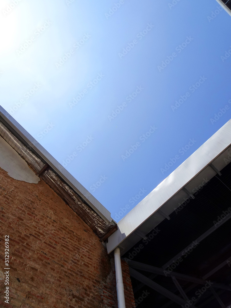 Red brick wall and metal roof of old factory with sun shines and blue sky 