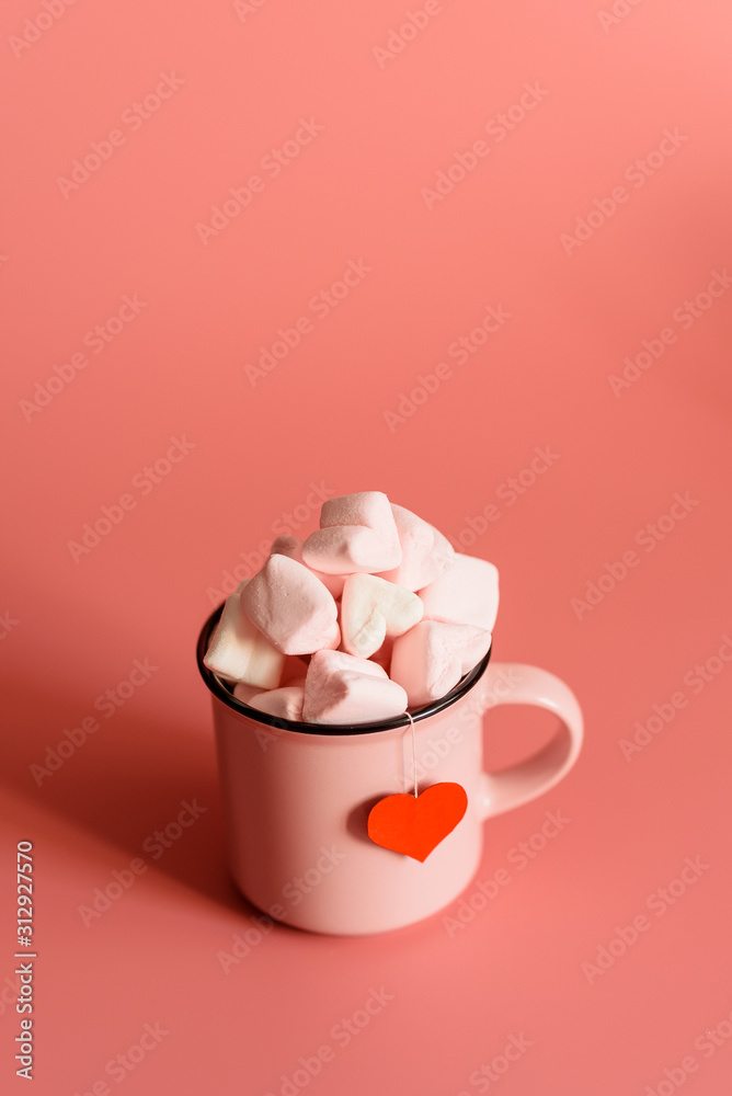pink mug on a pink background filled with marshmallows in the form of hearts. next to it is a box with a gift for Valentine's Day. valentine's day holiday concept pink mug on a pink background filled with marshmallows in the form of hearts. next to it is a box with a gift for Valentine's Day. valentine's day holiday concept
