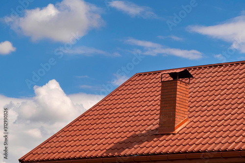 Part of the house with a brown tiled roof and a chimney against the sky. Metal roof.