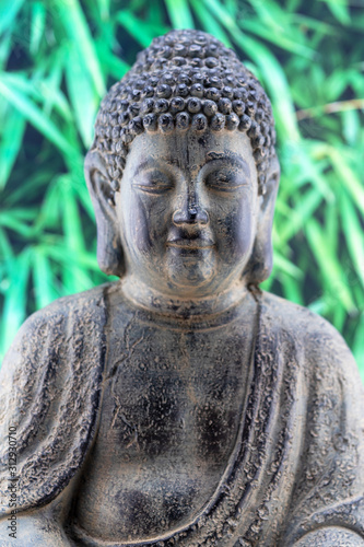 Porträt einer sitzenden Buddhafigur isoliert vor unscharfem Hintergrund aus Bambusblättern