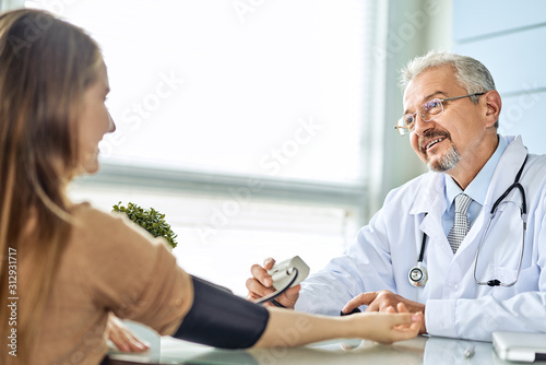 Young woman at the doctor appointment. The doctor measures the pressure of the patient