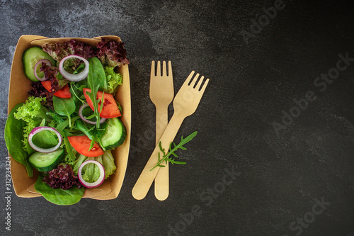 Healthy salad, leaves mix salad in paper disposable tableware (mix micro greens, cucumber, tomato, onion, other ingredients). food background. copy space