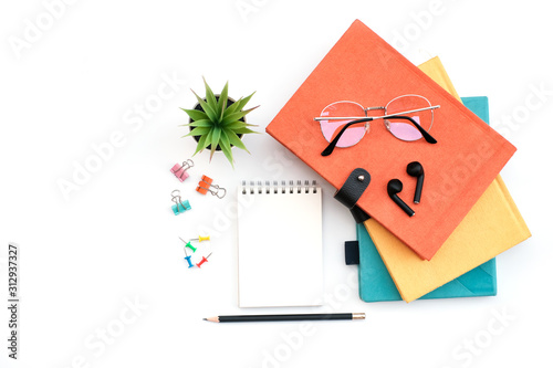 Flat lay black to school and education concept on white table desk with blank notepad and stack of book , green plant and supplies, ear phone and glass, Top view with copy space, work space